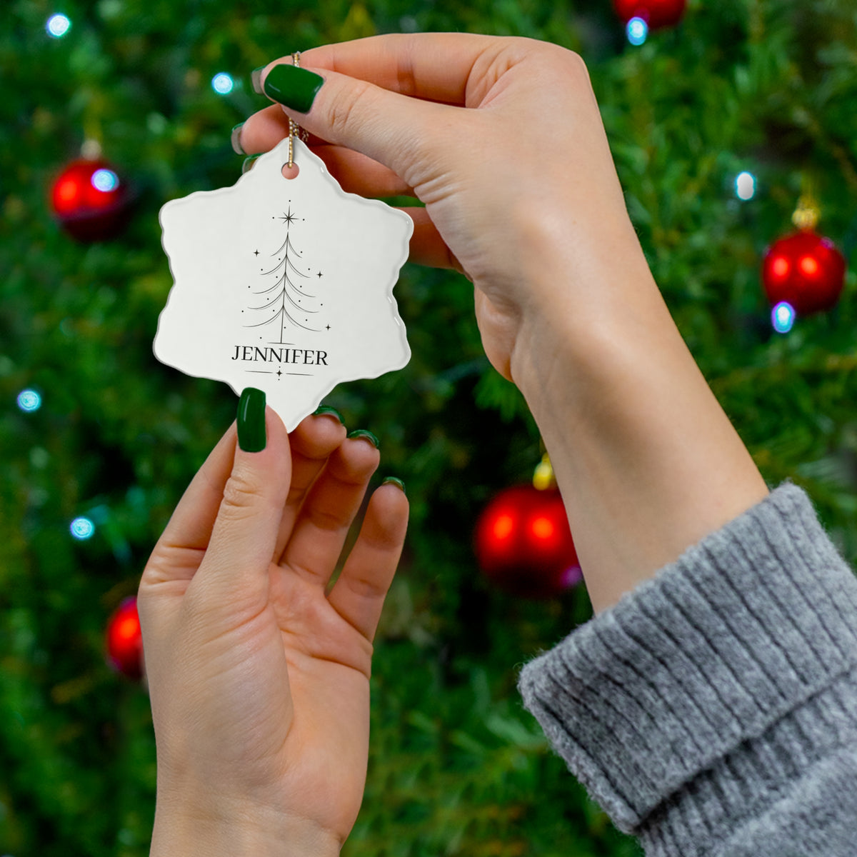 Hand holding a snowflake-shaped personalized Christmas tree ornament by the tree
