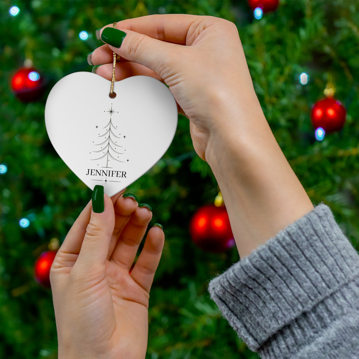 Hand holding a heart-shaped personalized Christmas tree ornament by the tree