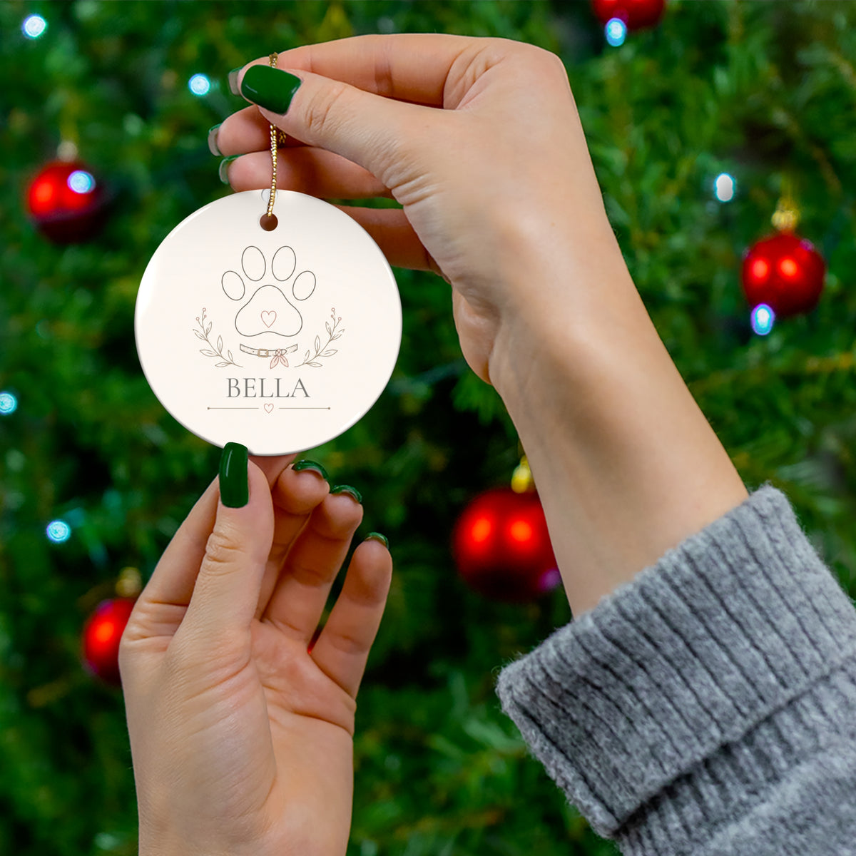 Hand holding a round personalized pet ornament in front of a Christmas tree